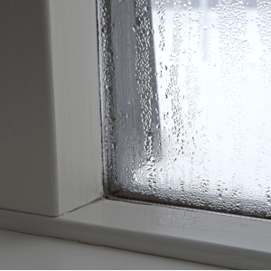 Nærbilde av kondens i et vindu. Vinduskarmen er våt av fukt.